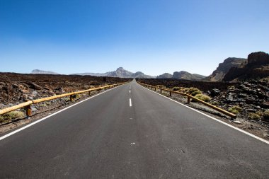 Taşları ve boş tabelaları olan ıssız bir yol. Ufuk olarak mavi gökyüzü ve asfalt bir yol perspektifinde düz