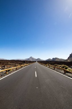 Taşları ve boş tabelaları olan ıssız bir yol. Ufuk olarak mavi gökyüzü ve asfalt bir yol perspektifinde düz