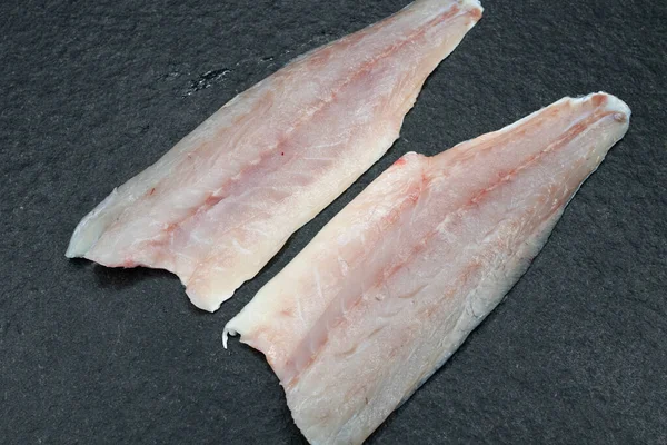 在木制桌子上和一块黑色花岗岩石板上的鱼片 新鲜的海鱼随时可以烹调 两半没有骨头的海底鱼片 图库照片