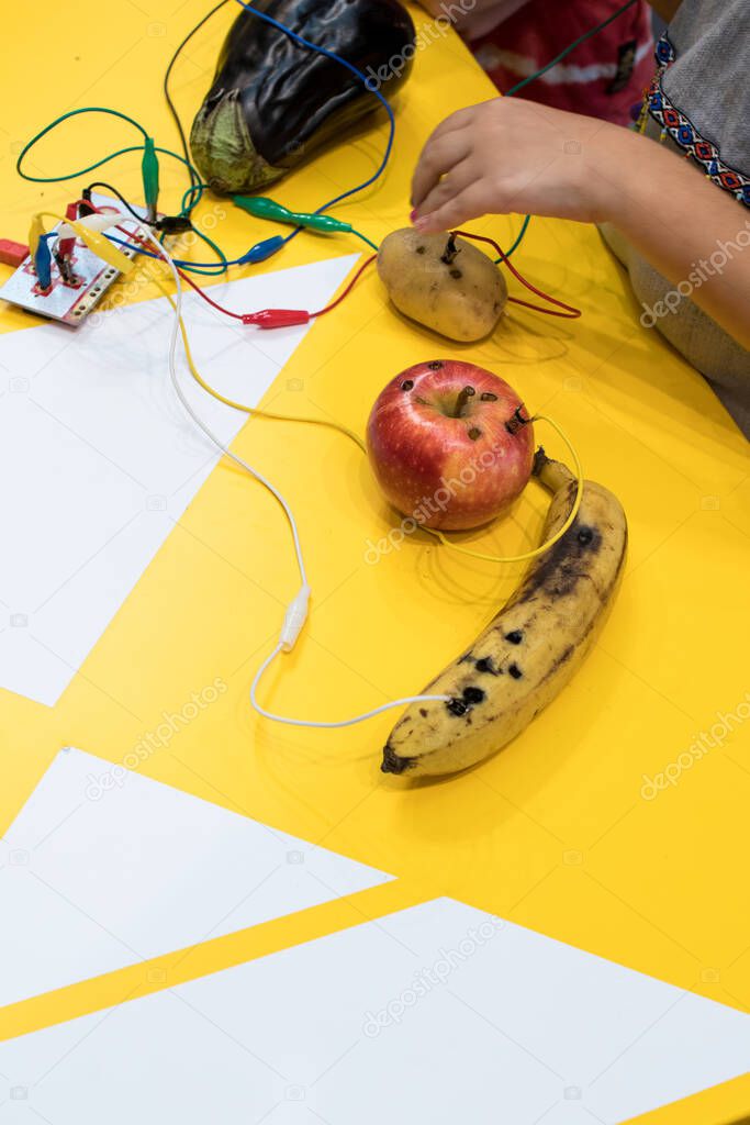 Fruit piano with kids. STEM education activity allow kids to play music with fruit and vegetables. Microcontroller converts keys in sound with some fruits. Yellow background and vegetables wired
