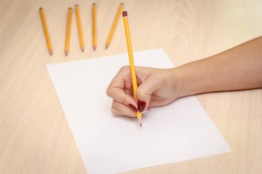 Ahşap masa arkasında kağıt üzerine kalem yazan bir kadın eli..