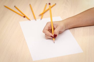 Ahşap masa arkasında kağıt üzerine kalem yazan bir kadın eli..