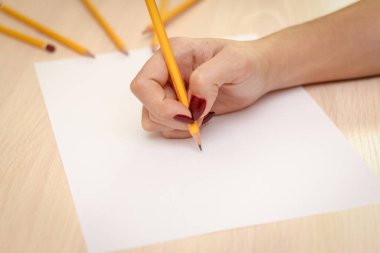 Ahşap masa arkasında kağıt üzerine kalem yazan bir kadın eli..
