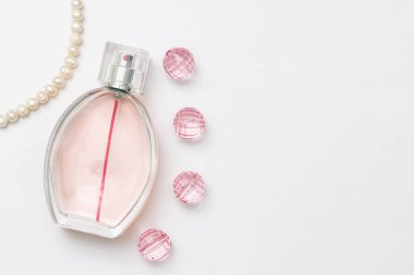 Bir şişe parfüm. İnci kolye, pembe kristaller ve açık beyaz arka plan üzerine basit bir metin için yer.