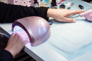 Manikür için ultraviyole lamba jeli. Güzellik salonundaki prosedür. Usta müşterinin tırnaklarını cila ile kaplar..