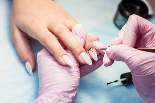 Close up manicure process. A professional manicurist glues rhinestones on nails.