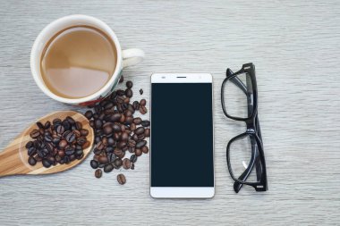 Bir fincan kahve, kahve çekirdeği ve ahşap bir masada akıllı telefon. 