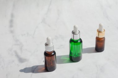 Yeşil ve kahverengi yüz maskesi esaslı yağ ya da beyaz mermer arka planda serum ambalajı. Cilt konsepti için güzellik kozmetik ürünü. Minimum ve lüks bir tarz. Işık ve gölge.