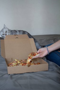 Asyalı bir kadın tatilde dinleniyor, yatakta oturuyor ve lezzetli bir pizza yiyor..