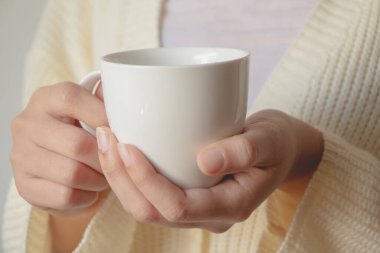 Kadın el ele tutuşan bir bardak içecek. Sabahları elinde çay ya da kahve tutan beyaz kazaklı güzel bir kız..  