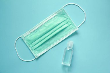 Mavi arka planda küçük bir antiseptik jel şişesi olan koruyucu tıbbi maske. el dezenfektanı. Hijyen, dezenfeksiyon ve sağlık konsepti.