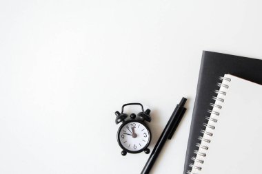 Siyah çalar saat, beyaz arka planda defter ve kalem var. Üst Manzara. Boşluğu kopyala.