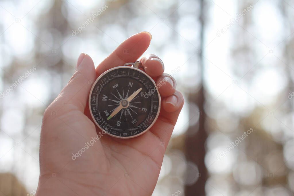 Close up of female hands holding compass against forest.