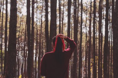 Ormanda arka planda çam ağacında kırmızı kurdeleli kırmızı kazak giyen bir kadın..