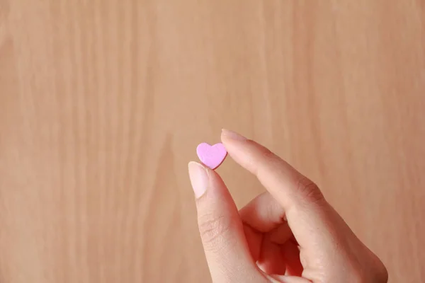 Woman holding tiny pink heart on wood background. love concept.