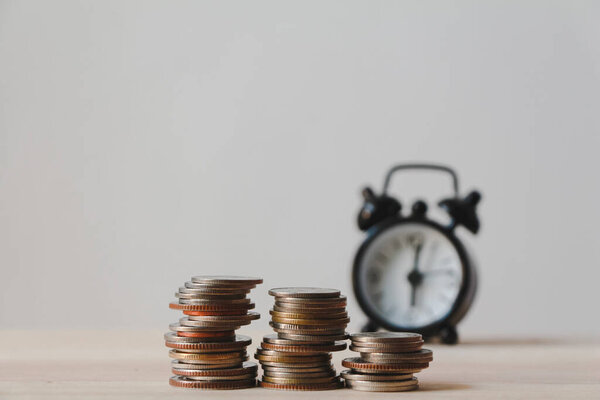 Coin stack and blurred alarm clock on wood table.business financial ideas concept