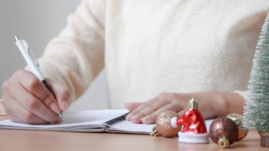 Defterine kalem yazan bir kadın. Masada Noel süsü.