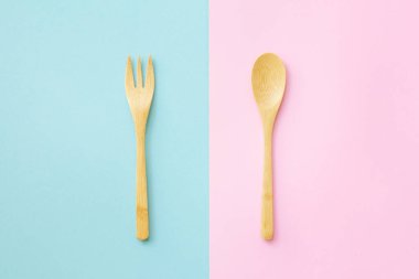 Pembe ve mavi arka planda plastik kaşıklı düz bir tahta kaşık vardı. Sürdürülebilir yaşam tarzı ve sıfır atık kavramı.