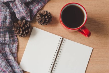 Kahveli defter, kozalaklı koni ve ahşap masa arkasında eşarp, ofis masası. Sonbahar ve kış.