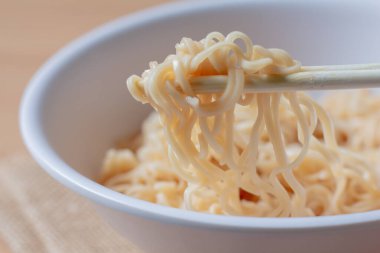 Beyaz kasede hazır erişte yiyen bir kadın..