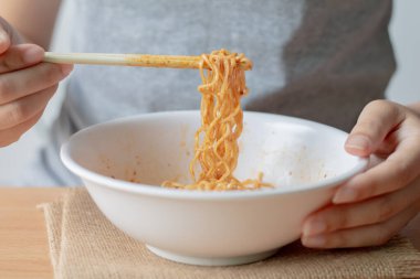 Beyaz kasede hazır erişte yiyen bir kadın..