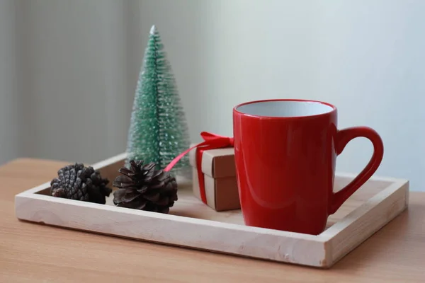 Red cup of hot chocolate with Christmas decoration and gift box in wooden box. Holiday concept.