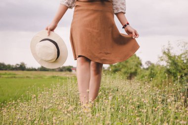Genç bir kadın çim çiçeğinde yürüyor. Eskimiş şapkalı kahverengi etek..