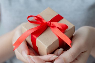 Kadının elinde kırmızı kurdeleyle sarılı küçük kahverengi bir hediye kutusu var. Alanın derinliği küçük kutuya odaklanmış..