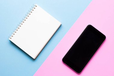 Mavi ve pembe renkli arka planda akıllı telefonlu defter. Asgari biçim.