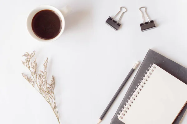 Kağıt defter, kalem, bir fincan kahve ve beyaz arka planda fotokopi alanı olan kuru çiçekler. Ofis masaüstü görünümü İskandinav stili.