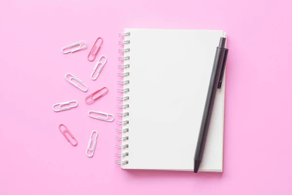 notebook and pen on pink background.