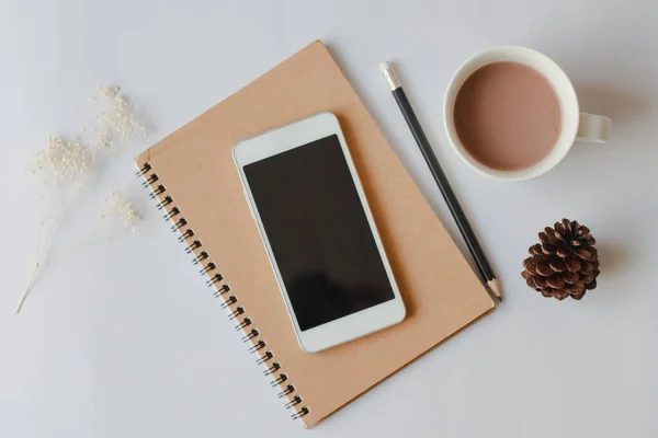 Akıllı telefon, defter, kalem, kahve ve fotokopi arkaplanı olan kuru çam kozalaklı ofis masasının düz bir fotoğrafı..