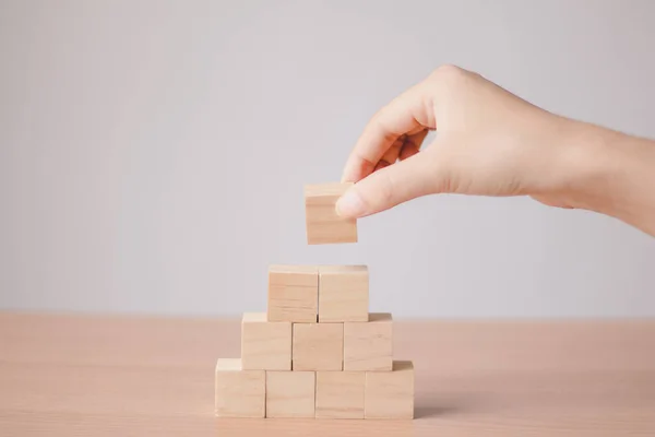 Hand putting wood cube on top of wood block stacking as step stair.business growth to success.