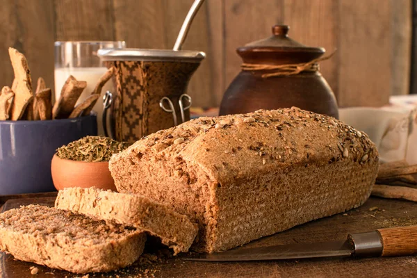 Pan casero de harina integral sobre base de madera y fondo de madera rustica con utensilios de cocina