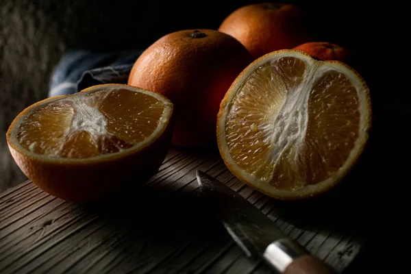 Ahşap tabanlı ve koyu arkaplanda bıçakla kesilmiş portakallar.