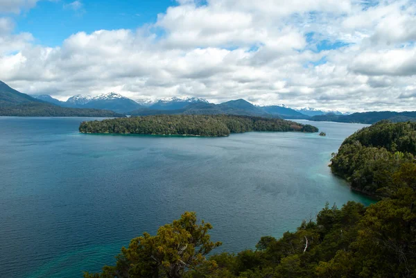 Patagonya Gölü, arka planda çam ormanları ve karlı dağlarla çevrili.