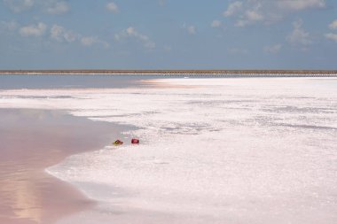 Pembe tuz gölü. Tuz endüstrisi - pembe tuzun çıkarılması. Doğanın mucizesi. Muhteşem bir manzara. Mavi gökyüzü ve bulutlar pembe suya yansıyor.