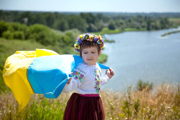 Счастливая улыбающаяся украинка на вышиванке с желтым и синим флагом на горе на фоне полей и реки. День независимости Украины. День Государственного флага Украины. 