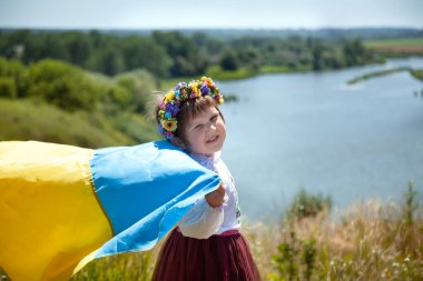 Vyshyvanka 'daki mutlu gülümseyen Ukraynalı kız tarlaların ve nehrin arkasındaki bir dağda sarı ve mavi bir bayrak taşıyor. Ukrayna 'nın Bağımsızlık Günü. Ukrayna Ulusal Bayrak Günü. 