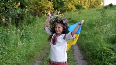 Ukrayna 'nın dalgalanan mavi ve sarı bayrağı küçük Ukraynalı kızın ellerinde. Geleneksel nakış işlemede gülümseyen çocuk (vyshyvanka) ve kır çiçeklerinden bir çelenk. Ukrayna 'nın Bağımsızlık Günü. Bayrak Günü