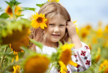 7 yaşında, gülümseyen Ukraynalı uzun sarı saçlı ve mavi gözlü geleneksel işlemeli gömlekli bir kız.