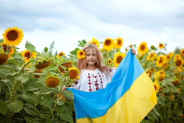 身穿传统绣花衬衫 手上拿着黄蓝色旗帜的乌克兰微笑女孩 她的手捧着一片向日葵 — 图库照片