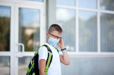 Back to school. Shoolboy in glasses wearing mask and backpacks protect and safety from coronavirus. Child going school after pandemic over. Standing near school. students are ready for new year. clipart