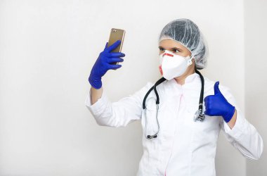 Steteskoplu doktor kadın, beyaz arka planda gözlüklü. Tıp önlüklü kadın doktor cep telefonuyla selfie çekiyor. Sağlık personeli, sağlık, tıp