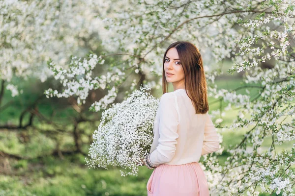 春に開花する木の果樹園でポーズをとる帽子の素晴らしい若い女性 春の庭で香りを楽しむ美しい幸せな若い女性 — ストック写真