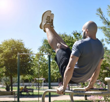 Jimnastik yapan ve halka açık bir parkta sokak antrenmanı yapan ve maske takan bir sporcu.