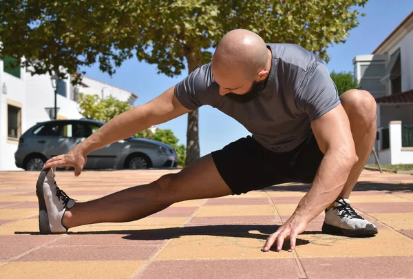 Fitness kaslı bir adam halka açık bir parkta bacak esnetiyor.