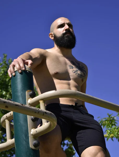 Spor salonundaki parmaklıklar üzerinde egzersiz yapan kaslı bir adam.