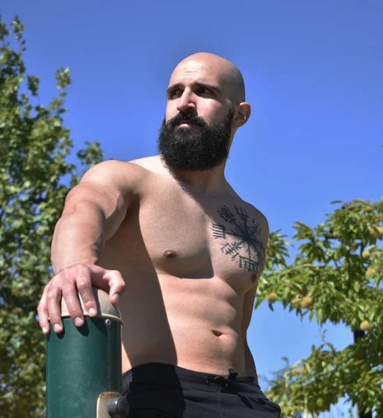 Halka açık bir parkta solda kaslı bir adam var.