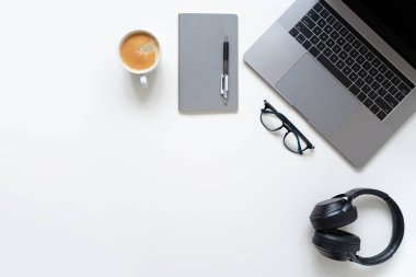 Merkez ofis. Laptop, bardaklar, kahve fincanı, defter ve kulaklıklar beyaz masada. Uzayı kopyala Yatay.